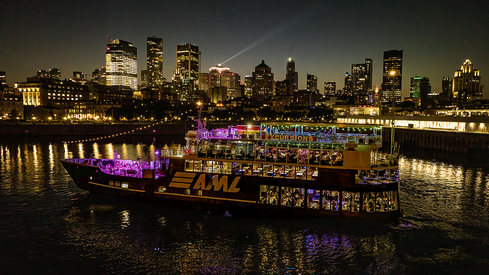 Aerial view of the AML Cavalier Maxim entering Montreal's Old Port at night, with the city skyline in the background.