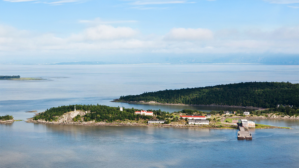 Vue aérienne de Grosse-Île et du fleuve Saint-Laurent. On peut y voir de la verdure et des bâtiments typiques de l'île.