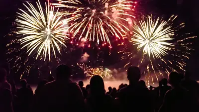 A crowd watches a spectacular fireworks display lighting up the night sky with golden and red bursts, creating a festive and magical atmosphere.