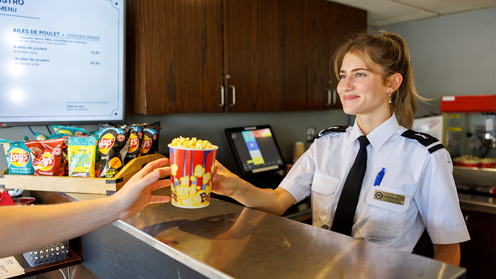A smiling waitress serving popcorn to a customer. Bistro on board the AML Louis Jolliet in Quebec City