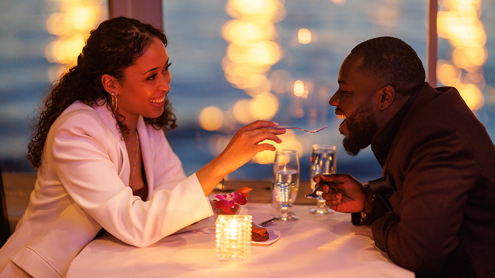 Un couple romantique et souriant dégustant un repas bistronomique avec vue sur les lumières de la ville