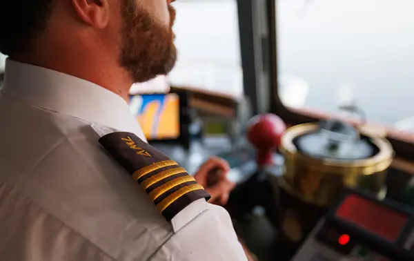 Close-up of a captain in uniform with gold stripes on the shoulder, in the control room of a ship, surrounded by navigation equipment and instruments.