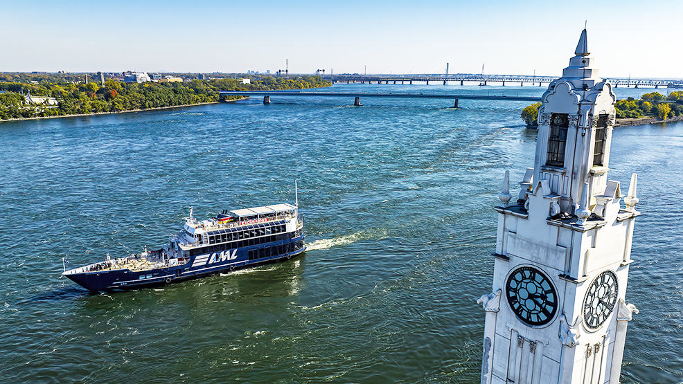 The AML Cavalier Maxim ship sailing on the Saint Lawrence River with the Montreal Clock Tower in the foreground and the Saint Helen's Island and the Samuel de Champlain Bridge in the background