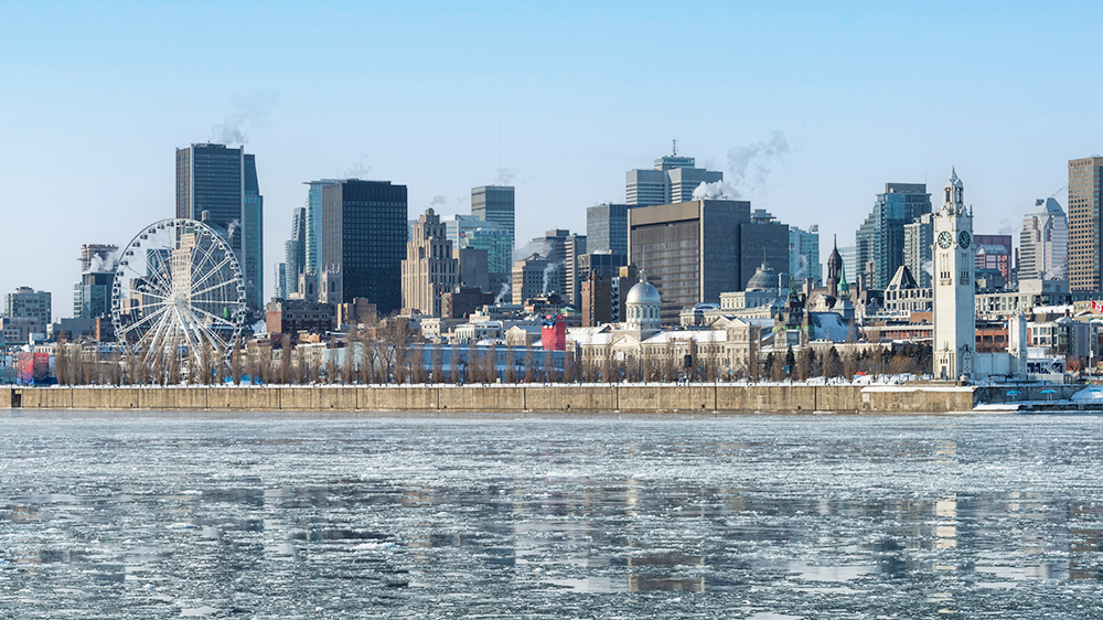 Paysage du Vieux Port de Montréal en hiver avec vue sur la grande roue, le fleuve Saint-Laurent gelé au premier plan et la skyline de la ville en arrière plan.