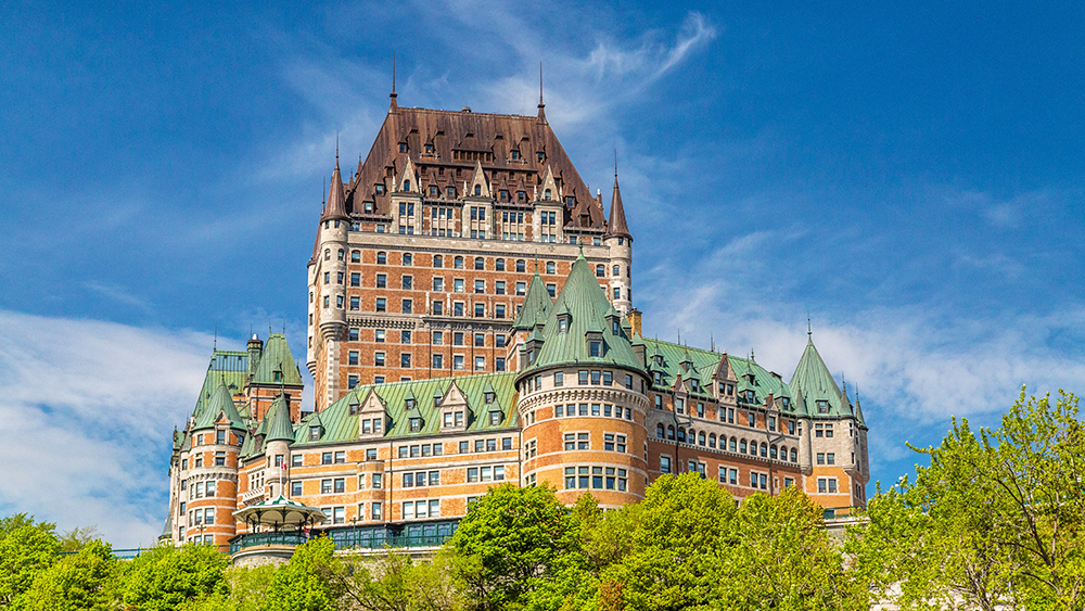  The Château Frontenac in Quebec City standing majestically against a blue sky and lush greenery.