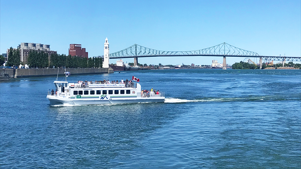 Montreal river shuttle sailing on the Saint Lawrence River with the clock tower and Jacques Cartier Bridge in the background