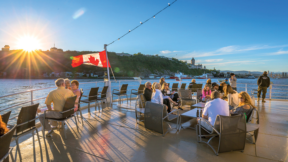 View of one of the terraces of the AML Louis Jolliet ship with customers seated and enjoying the fresh air, with a view of the Château Frontenac and Cap Diamant in the background