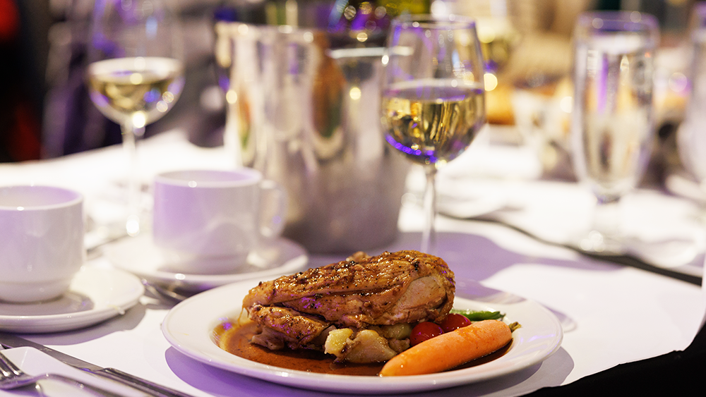 Une assiette bistronomique comprenant un suprême de volaille manchon, des pommes de terre grelots et des légumes frais du marché accompagné d'un verre de vin blanc.
