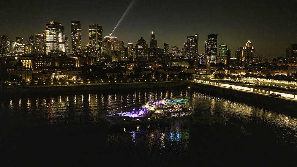 Aerial view of the AML Cavalier Maxim parked in Montreal's Old Port at night, with the city skyline in the background.