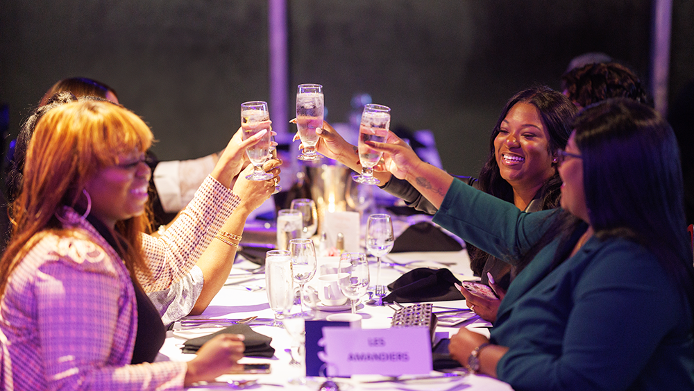 A group of smiling women clinking champagne glasses at a table during a dinner cruise aboard the AML Cavalier Maxim in Montreal.