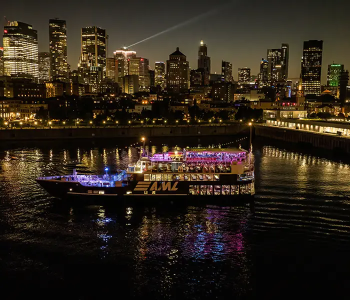 A stunning nighttime view of an illuminated cruise ship sailing on a river, with a sparkling city skyline in the background featuring skyscrapers and urban lights.