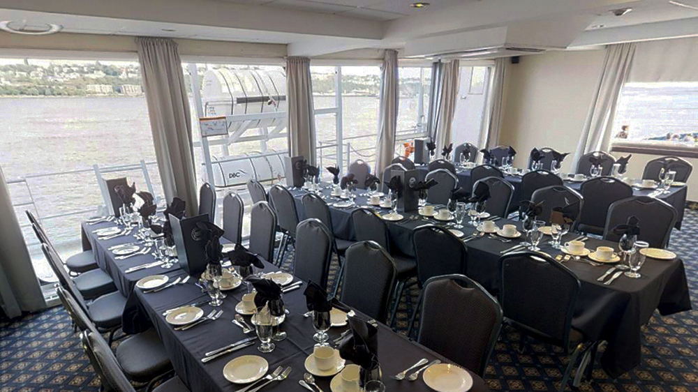 Captain's lounge of the AML Louis Jolliet ship in Quebec, set up with tables for guests with a view of the Saint Lawrence River through the window.