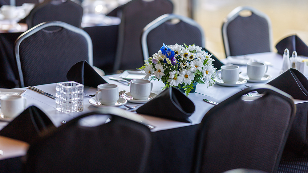Gros plan sur une table dressée, avec des assiettes, des verres, des couverts, et un beau bouquet blanc et bleu en guise de décoration
