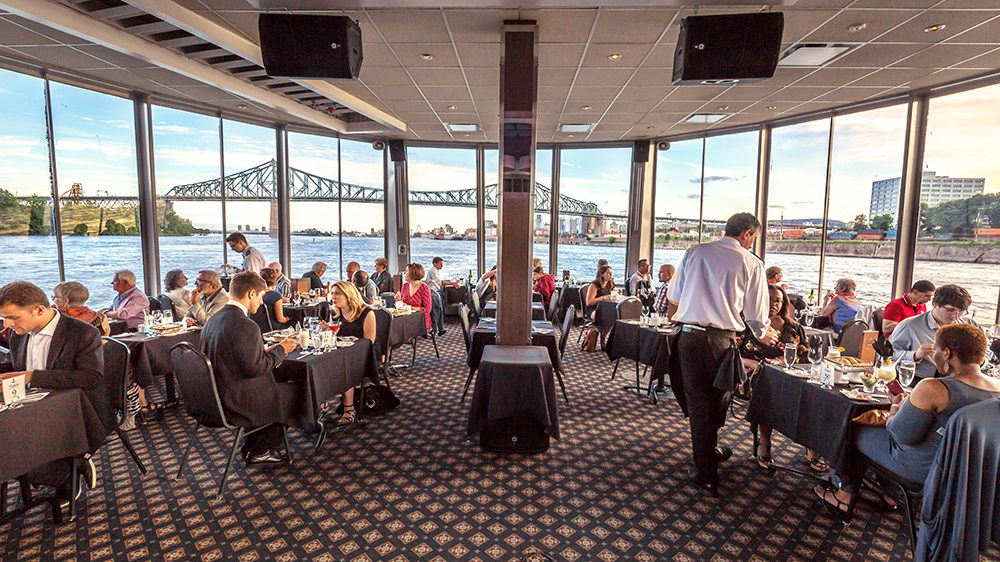 Main room of the boat with large windows where customers dine while admiring the view of the St. Lawrence River