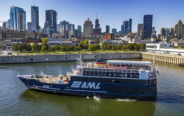 A large black cruise ship with "AML" written on it, sailing on a river. In the background, a Ferris wheel, autumn trees, and urban buildings under a clear blue sky.
