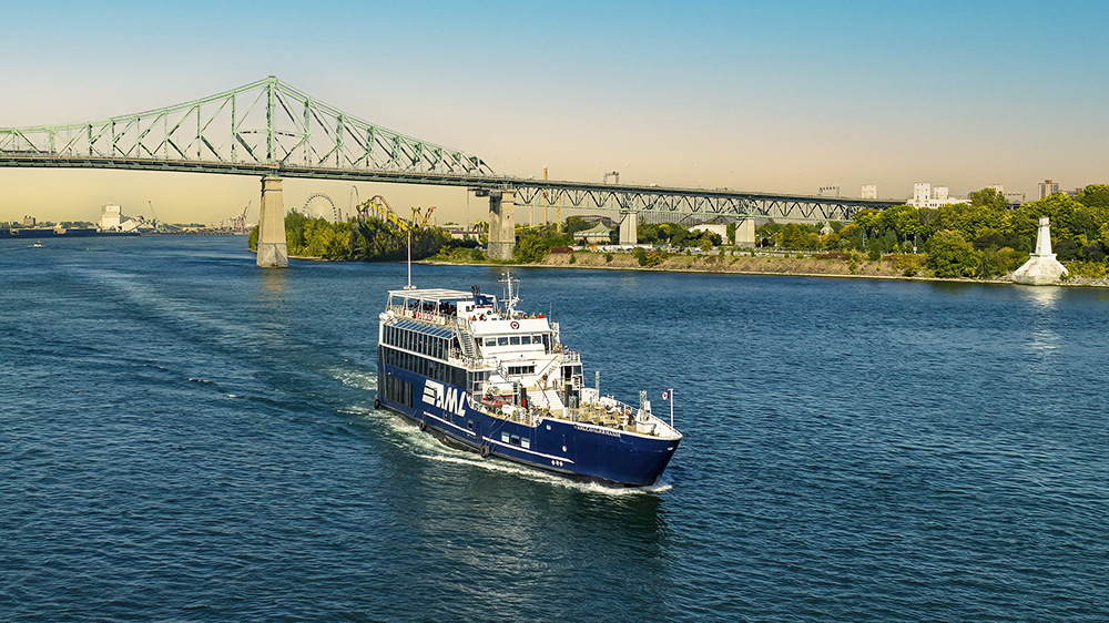 Le navire AML Cavalier Maxim au premier plan naviguant sur le fleuve Saint-Laurent avec une vue sur le Pont Jacques Cartier en arrière plan.