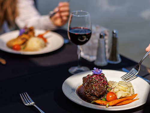 Assiette comprenant un repas bistronomique de viande grillée avec des légumes frais du marché accompagné d'un verre de vin rouge