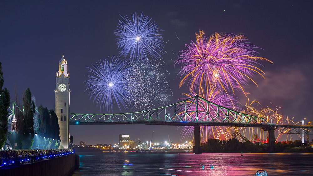 View of the clock tower and the Jacques Cartier Bridge in Montreal with fireworks overlooking the monuments