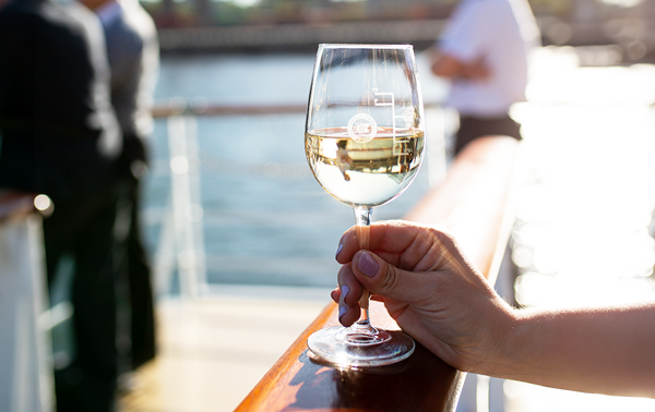 Une main en gros plan tenant un verre de vin blanc sur une des terrasses du navire à Montréal.