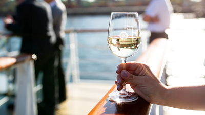 Une main en gros plan tenant un verre de vin blanc sur une des terrasses du navire à Montréal.