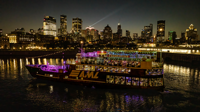 Aerial view of the AML Cavalier Maxim entering Montreal's Old Port at night, with the city skyline in the background.