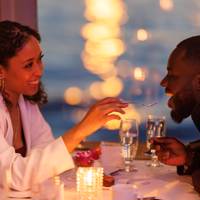 A romantic and smiling couple enjoying a bistronomic meal with a view of the city lights.