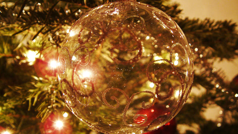 Boule de Noël transparente et dorée en gros plan suspendue à un sapin.