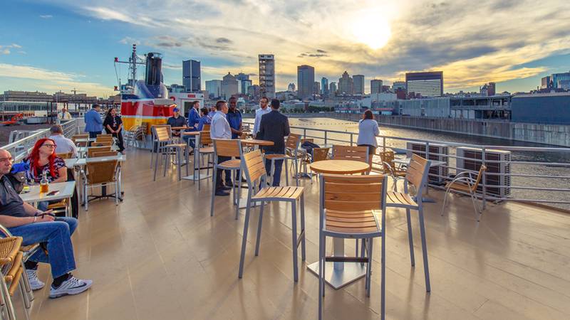 Outdoor terrace on the upper deck of the AML Cavalier Maxim with guests seated at tables enjoying the view of the Montreal skyline.