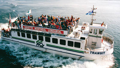 A river shuttle filled with passengers enjoying a ride between Montreal and Longueuil on calm waters, with flags waving on the boat.