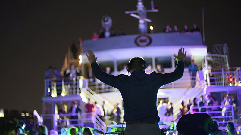 Un DJ anime une soirée éclectique avec une foule qui danse sur l'une des terrasses du navire AML Cavalier Maxim à Montréal