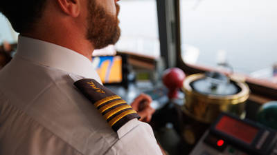 Close-up of a captain in uniform with gold stripes on the shoulder, in the control room of a ship, surrounded by navigation equipment and instruments.