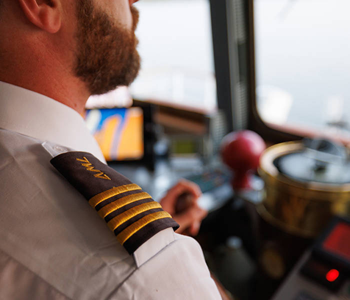 Close-up of a captain in uniform with gold stripes on the shoulder, in the control room of a ship, surrounded by navigation equipment and instruments.