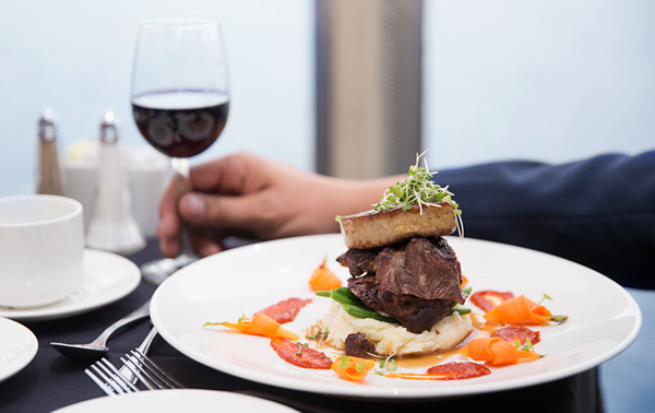 Une assiette de plat bistronomique comprenant un plat de bœuf joliment servi avec des légumes frais du marché, accompagné d'un verre de vin rouge.