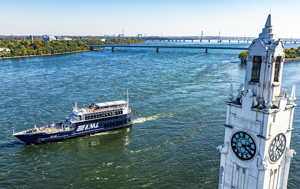 Le navire AML Cavalier Maxim naviguant sur le fleuve Saint-Laurent avec au premier plan la tour de l'horloge de Montréal et en arrière plan l'Ile Sainte Hélène et le Pont Samuel de Champlain