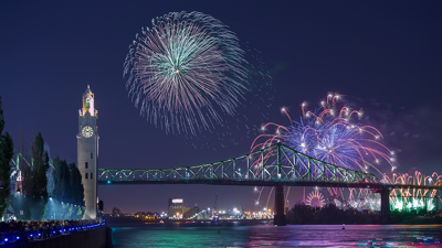View of the clock tower and the Jacques Cartier Bridge in Montreal with majestic fireworks overlooking the monuments