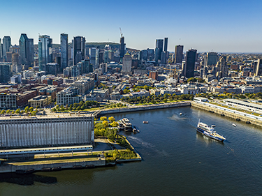 Aerial view of the AML Cavalier Maxim ship leaving the Old Port of Montreal, with a view of the city in the background under a blue sky.
