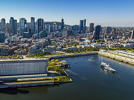 Aerial view of the AML Cavalier Maxim ship leaving the Old Port of Montreal, with a view of the city in the background under a blue sky.