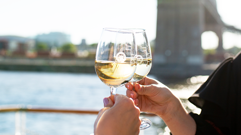 Deux mains trinquant avec deux verres de vin blanc sur l'une des terrasses du navire à Montréal.