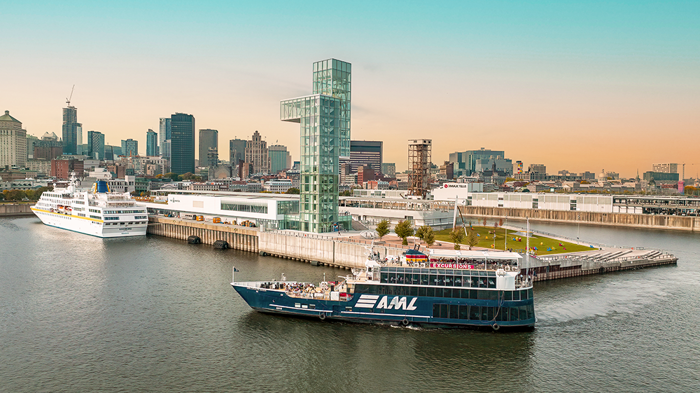 Aerial view of the AML Cavalier Maxim entering Montreal's Old Port at night, with a view of the city skyline in the background.