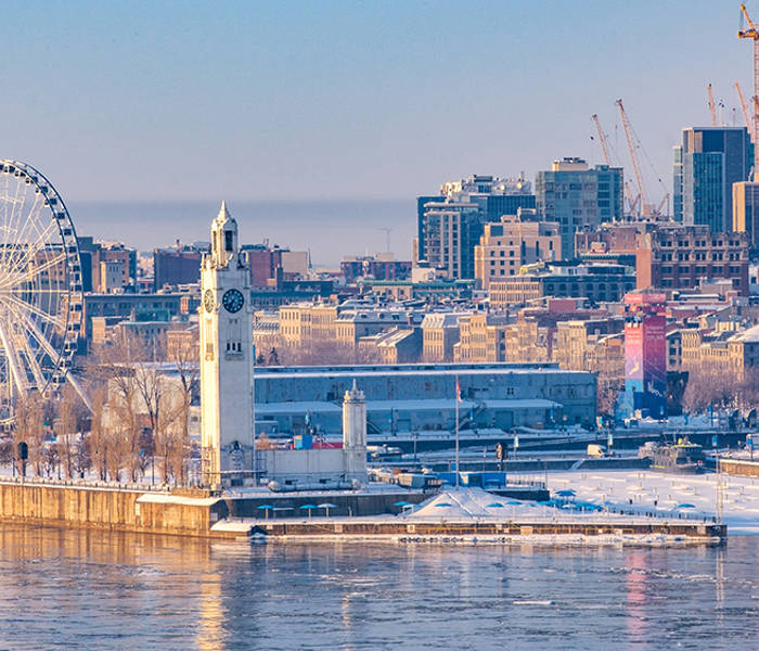 Panoramic view of Old Port of Montreal in winter, featuring the Clock Tower, the Ferris wheel, and downtown buildings under a clear sky.