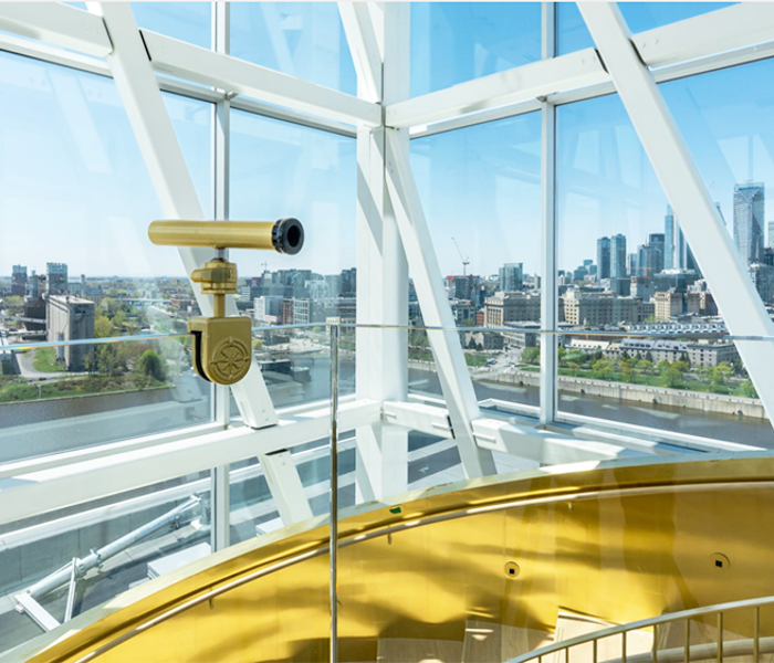 Un télescope dans un observatoire moderne doté de fenêtres panoramiques donnant sur la skyline de Montréal sous un ciel bleu.