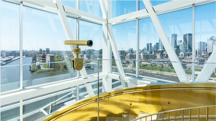 A telescope in a modern observatory with panoramic windows overlooking the Montreal skyline under a blue sky.