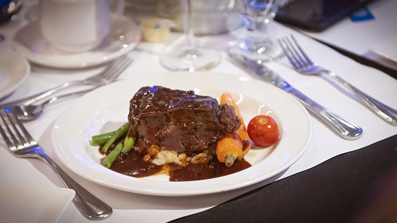 Une assiette comprenant un succulent plat de bœuf, garni de haricots verts, d'une tomate rôtie et d'un accompagnement de pommes de terre en gros plan.
