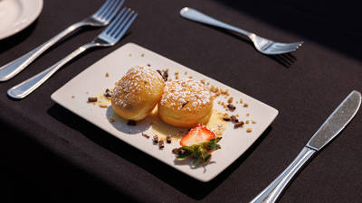 A plate of delicious desserts featuring two donuts dusted with powdered sugar, garnished with sauce, a strawberry, and chocolate pieces.