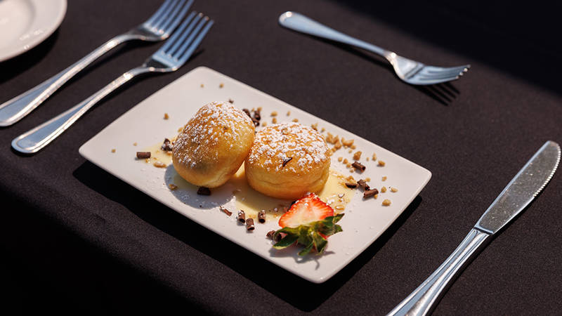 A plate of delicious desserts featuring two donuts dusted with powdered sugar, garnished with sauce, a strawberry, and chocolate pieces.