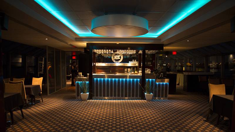 Vue de la salle du Pont C avec le bar illuminé en bleu au fond et les tables de chaque côté de la salle