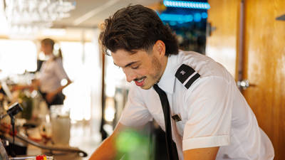  A bartender in a white uniform with a black tie prepares a drink in a bright and modern bar, creating a professional and welcoming atmosphere.