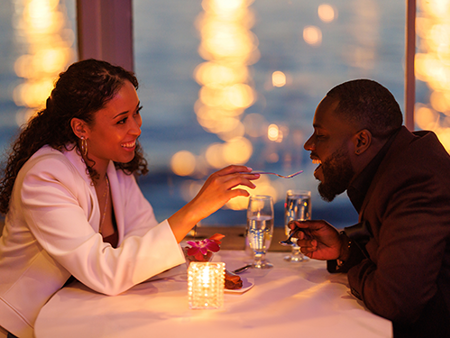 A romantic and smiling couple enjoying a bistronomic meal with a view of the city lights.