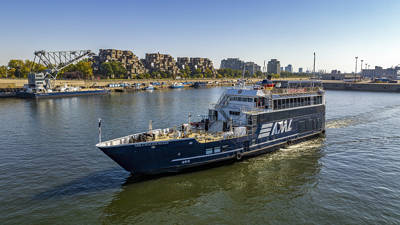 A black cruise ship with "AML" written on it, sailing on a river. In the background, a distinctive residential complex, a bridge, and urban buildings under a clear blue sky.