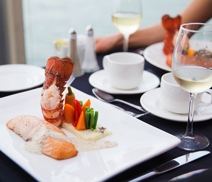 Un plat gastronomique comprenant un pavé de saumon, une queue de homard et des légumes frais du marché dressé dans une assiette élégante.